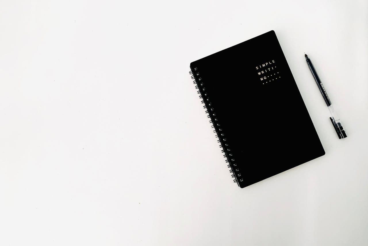 Sổ tay màu đen và bút trên nền trắng tối giản - chuẩn bị viết WHY statement cho thương hiệu